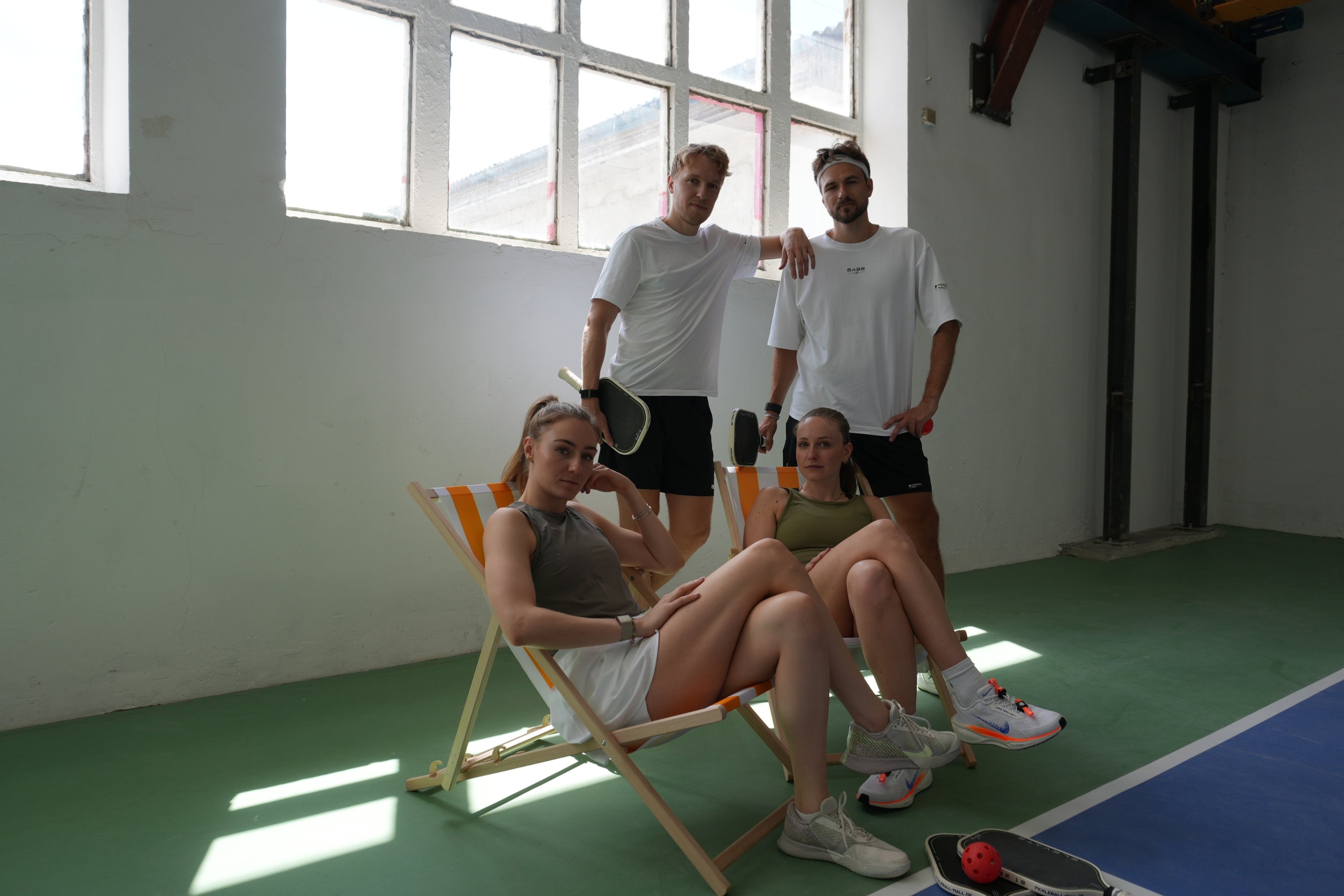 Team von Pickleball-Mall auf einem Indoor-Pickleball-Court; zwei Personen sitzen, zwei stehen mit Pickleball-Schlägern.