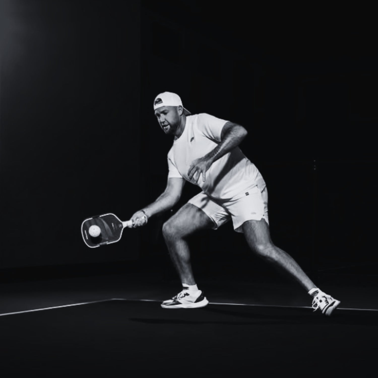 Pickleball-Spieler in sportlicher Aktion auf dem Court, in heller Kleidung und mit Paddle von Selkirk, während er einen tiefen Ball mit einer Vorhand erreicht.